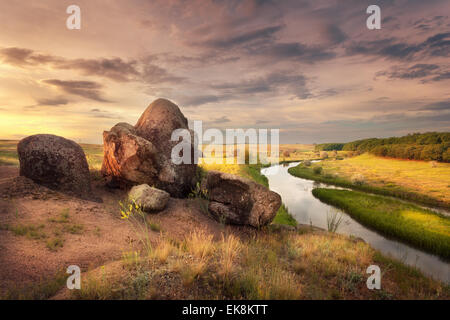 Schönen Sommer Sonnenuntergang am Fluss mit orangefarbenen Himmel, Wolken, Felsen, gelbe Rasen, Blumen und Wasser mit Reflexion. Ukraine Stockfoto