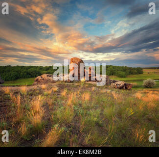 Schönen Sommer Sonnenuntergang mit blauem Himmel, gelb orange Wolken, Felsen, Rasen und grüne Bäume in der Ukraine Stockfoto