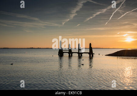 Sonnenuntergang in der Nordsee mit Linien von Flugzeugen am Himmel und Holzkonstruktion im Wasser Stockfoto