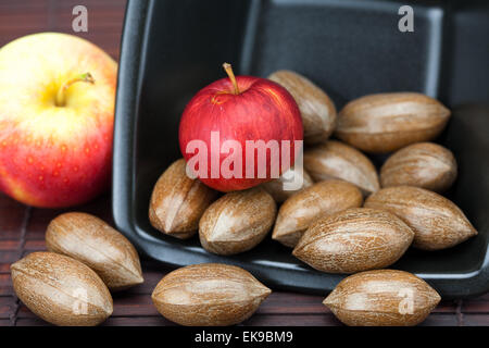 Pekannüsse und Äpfel in einer Schüssel auf einer Bambusmatte Stockfoto