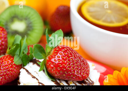 Tee mit Zitrone, Mandarine, Kiwi, Kuchen und Erdbeeren liegen auf der ora Stockfoto