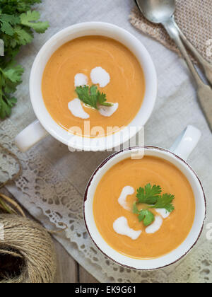 Zwei weiße Tassen mit Vegan (vegetarisch) Kürbis Creme Suppe mit Kokosmilch, serviert mit Petersilie. Draufsicht. Stockfoto