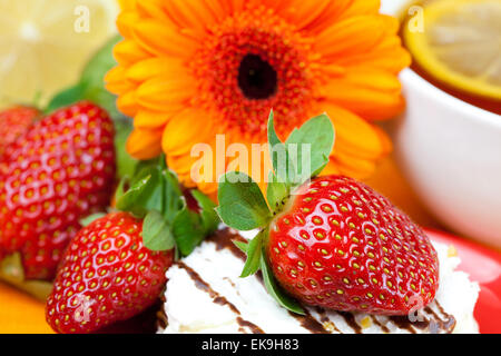 Tee mit Zitrone, Gerbera, Kuchen und Erdbeeren liegen auf der orange i Stockfoto