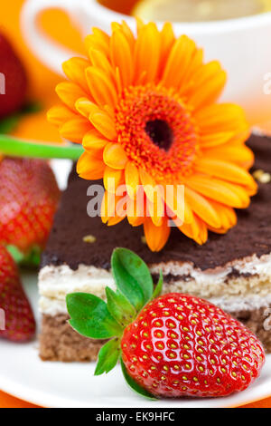 Gerbera, Zitronen-Tee, Kuchen und Erdbeeren liegen auf der orange fa Stockfoto