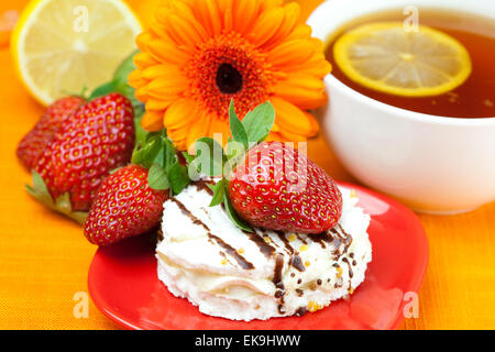 Tee mit Zitrone, Zitrone, Gerbera, Kuchen und Erdbeeren liegen auf der oran Stockfoto