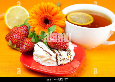 Tee mit Zitrone, Zitrone, Gerbera, Kuchen und Erdbeeren liegen auf der oran Stockfoto