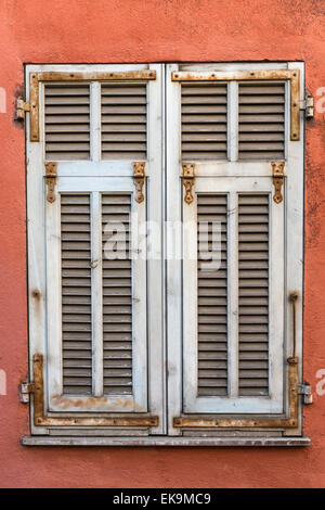 Weiße verwitterte französischen hölzernen Fensterläden auf einer roten Wand Stockfoto