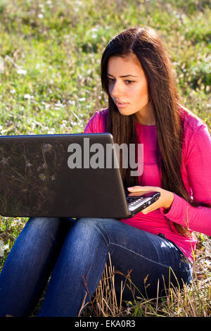 junge schöne Frau mit einem Laptop sitzt im Feld auf sky Stockfoto