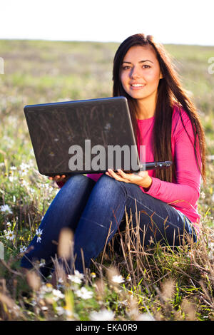 junge schöne Frau mit einem Laptop sitzt im Feld auf sky Stockfoto