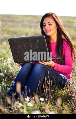 junge schöne Frau mit einem Laptop sitzt im Feld auf sky Stockfoto