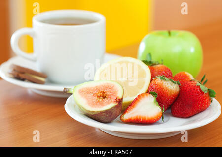 Tasse Tee, Cookie, Apfel, Zitrone, Feigen und Erdbeeren auf einem Teller Stockfoto