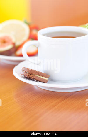 Tasse Tee, Cookie, Apfel, Zitrone, Feigen und Erdbeeren auf einem Teller Stockfoto