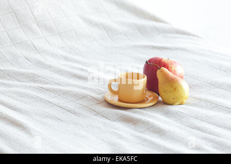 Tasse Tee, Apfel und Birne auf dem Bett Stockfoto