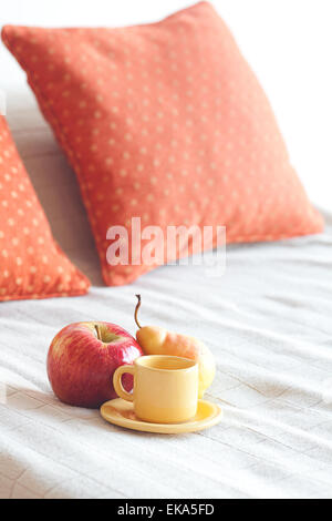 Tasse Tee, Apfel und Birne auf dem Bett Stockfoto