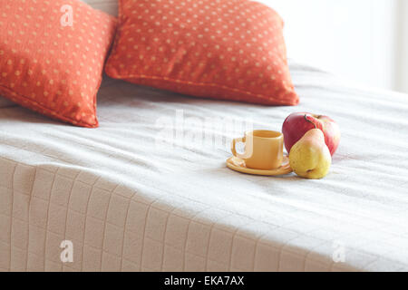 Tasse Tee, Apfel und Birne auf dem Bett Stockfoto