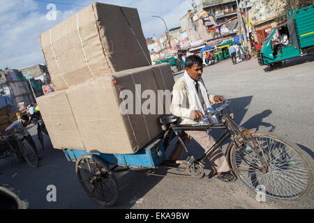 Ein Mann schleppt eine schwere Last von Fracht auf einem Wagen auf der Rückseite von seinem Fahrrad durch die Straßen von Delhi Stockfoto