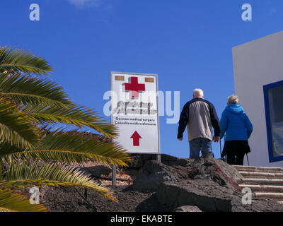 Medizinische Behandlung für die Krankheit im Ausland älteres Ehepaar und Zeichen für die lokale private Klinik Pflege in Kanaren Spanien EU mit blauem Himmel & Palmen Stockfoto