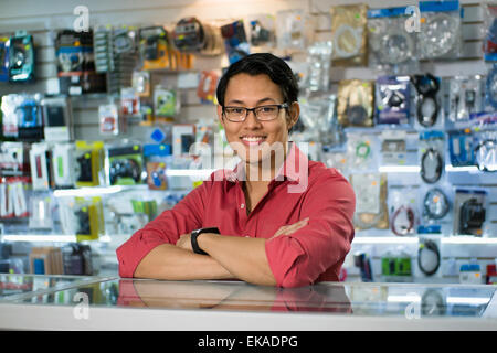 Porträt des jungen chinesischen Mann arbeitet als Angestellter in Computer und Technik Shop, lächelnd in die Kamera und stützte sich auf Schreibtisch im shop Stockfoto