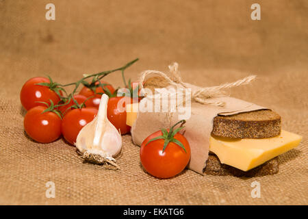 Sandwich mit Käse eingewickelt in Papier, Cherry-Tomaten und Knoblauch auf Tuch Stockfoto