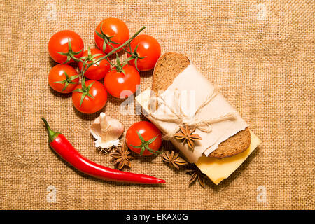 Sandwich mit Käse eingewickelt in Papier, Chili-Pfeffer, Cherry-Tomaten und Knoblauch auf Tuch Stockfoto