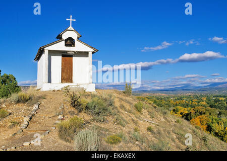 Eingerahmt von den entfernten schneebedeckten Sangre de Cristo Mountains, die winzigen Santa Rita Chapel steht auf einem Hügel. Stockfoto