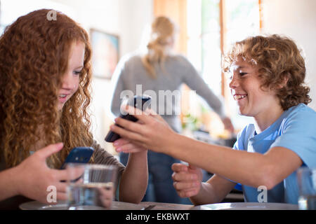 Geschwister mit Smartphone am Esstisch Stockfoto