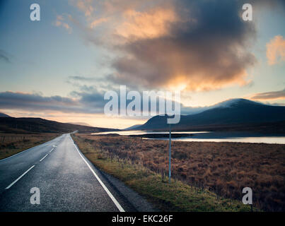 Blick auf ländliche Loch Road bei Sonnenuntergang, Assynt, North West Highlands, Schottland, Vereinigtes Königreich Stockfoto