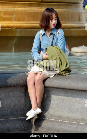 London, England, Vereinigtes Königreich. Japanische Frau sitzen von einem Brunnen am Trafalgar Square Stockfoto