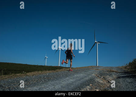 Mitte erwachsener Mann Joggen auf der Straße Windkraftanlagen Sie in Ferne Stockfoto