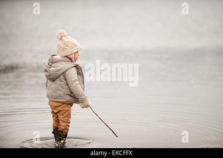 Kleiner Junge in einem See stehen, hält einen Stock Stockfoto