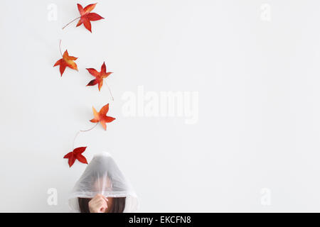 Herbstblätter fallen auf eine Frau im Regenmantel Stockfoto