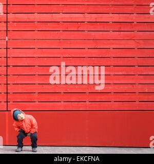 Junge in rot, der vor einer roten Wand herumwirrt Stockfoto