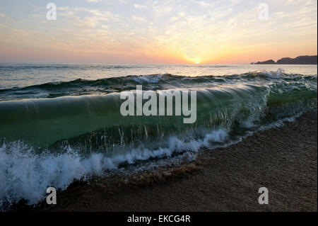 Eine Welle ist brechen und Rollen am tropischen Strand mit Sonnenuntergang im Hintergrund. Stockfoto