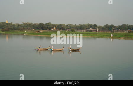 Drei Fischerboote gleiten auf dem ruhigen Wasser eines Sees in Myanmar an der Küste, an denen Menschen in den Bereichen arbeiten Stockfoto