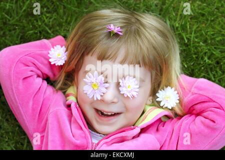 kleines Mädchen verlegen Rasen Daisiy Blumen in Augen Stockfoto