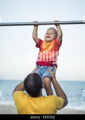 Vater hilft Baby an einer Klimmzugstange hängen Stockfoto