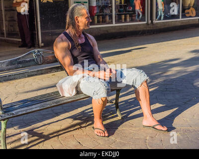 Eine 30er Jahre kubanische männlich mit Dreadlocks sitzt auf einer Bank der Stadt auf einem Bürgersteig in Havanna und raucht eine Zigarette im späten Nachmittag Licht. Stockfoto