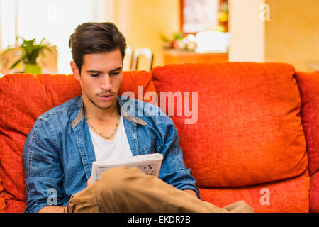 Junger Mann tun ein Kreuzworträtsel nachdenklich betrachtet man Magazin Stockfoto