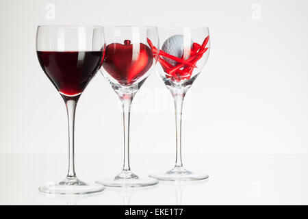 Weingläser mit roten Wein, Herz und Golf Ball auf weißen Tisch Stockfoto