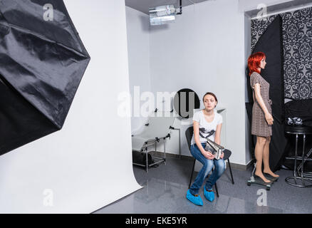 Ernste junge Frau in Freizeitkleidung, sitzend auf einem Stuhl im Fotostudio und etwas warten. Stockfoto