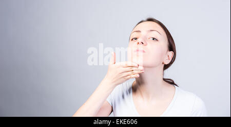 Junge Frau kippen ihren Kopf während heben ihr Kinn und man die Kamera ernst. Aufgenommen im Studio auf einem grauen Hintergrund Stockfoto