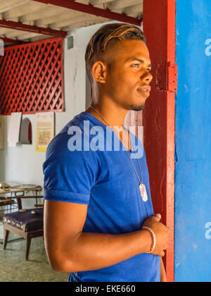 Eine zwanzig steht etwas Afro-kubanischen Mann in eine sehr bunte rote Tür mit einer blauen Wand, die die Farbe seines Hemdes entspricht. Stockfoto