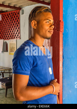 Eine zwanzig steht etwas Afro-kubanischen Mann in eine sehr bunte rote Tür mit einer blauen Wand, die die Farbe seines Hemdes entspricht. Stockfoto