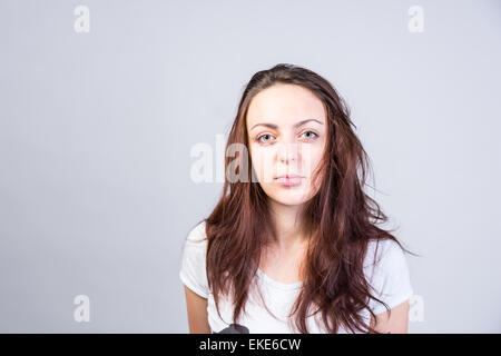 Schließen Sie ernste junge Frau mit langen chaotisch braun Haar Blick in die Kamera auf einem grauen Hintergrund. Stockfoto