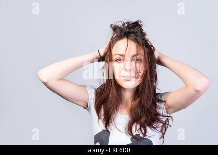 Nahaufnahme junge Frau hält ihr lange unordentlich Haare während Blick auf Kamera ernsthaft auf einem grauen Hintergrund. Stockfoto