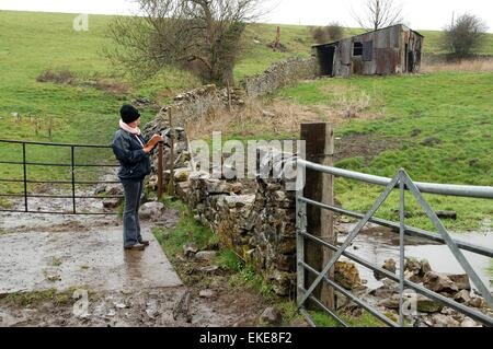 Frau beim Lesen einer Karte in Regen und Schlamm, Peak District, Derbyshire, Großbritannien Stockfoto