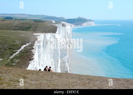 Menschen, die auf den Kreidefelsen der Seven Sisters, East Sussex, England, Großbritannien sitzen Stockfoto