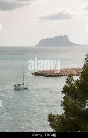 Eine Segelyacht tritt in den Hafen von Moriara an der Costa Blanca in Spanien mit Ifach Felsen im Hintergrund Stockfoto