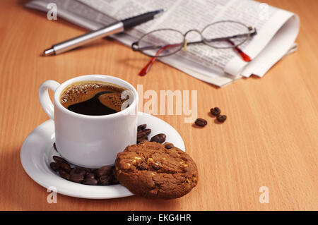 Tasse heißen Kaffee mit Schoko-Cookie und Zeitung auf Tisch Stockfoto