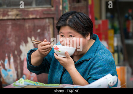 Frau hat Schüssel Nudeln am Bürgersteig stand im alten ummauerten Stadt Pingyao, Shanxi Provinz, China. Stockfoto